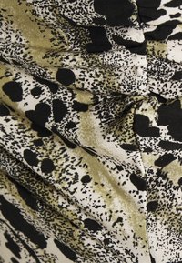 Nahaufnahme eines Stoffes mit abstraktem schwarz-olivgrün gesprenkeltem Muster auf beigem Hintergrund, Falten und Textur sichtbar.