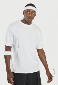 T-shirt en coton blanc à manches courtes, col rond et coupe décontractée. Associé à un bandeau blanc sur le bras et un short noir.