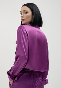 Lila satinierte kurze Jacke mit langen Ärmeln und Kragen, die eine glatte Textur und einen lockeren Schnitt aufweist, von hinten betrachtet.