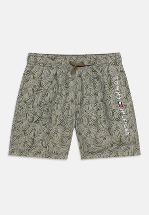 Olivovo zelené plavkové šortky s tmavým listovým vzorom, elastickým pásom so sťahovacou šnúrkou a bielym nápisom „Tommy Hilfiger“ s logom na pravej nohe.