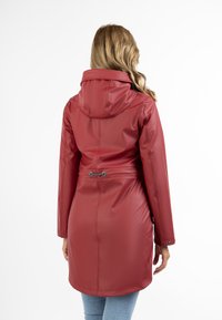 Red waterproof coat with a hood, cinched waist design, smooth texture, and snap button accents. Back view shows a fitted silhouette.