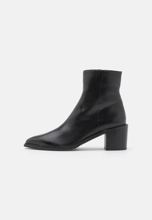 Bottine noire en cuir lisse, dotée d'un bout pointu et d'un talon épais. Le design est minimaliste avec des lignes épurées et sans embellissements visibles.