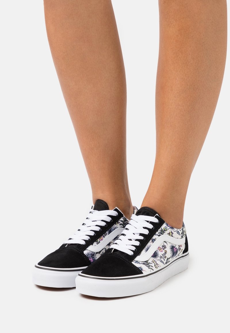 Svart mocka och mönstrad tygsneaker med vita snörningar, gummisula och sidodetaljer. Har ett blommigt mönster på sidopanelerna.