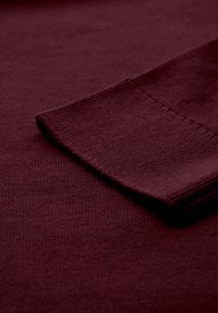 Burgundy stickad tygprov visar en jämn textur med en ribbad kant, med en ren finish och inga synliga mönster eller accenter.