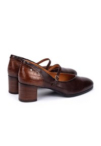 Chaussures Mary Jane en cuir marron foncé avec texture crocodile sur le talon, bout rond, sangle à boucle et talons carrés sur fond blanc.