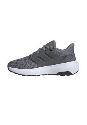 Zapatilla deportiva gris con parte superior de malla, tres franjas prominentes, suela blanca acolchada y suela negra. Presenta un sistema de cordones y un collar acolchado.