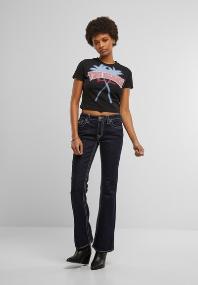 T-shirt noir court avec un graphisme coloré, associé à un jean évasé foncé avec des coutures contrastées et une fermeture par bouton. Bottines noires.