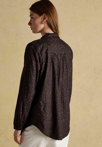 Black button-up shirt with a scattered pattern of rust and beige dots, featuring a collared neckline and pleated back detail.