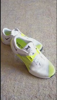 White athletic shoes with a mesh upper, featuring neon yellow accents, a textured sole, and a black Nike logo on the side.