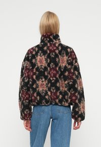 Vzorovaná fleecová bunda s vysokým límcem, černá, růžová a vínová barva, s uvolněným střihem a texturovanou, nadýchanou tkaninou.