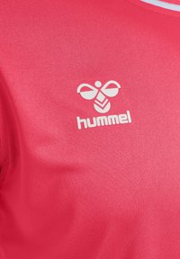 Röd sporttröja gjord av mjukt, lätt material med en vit Hummel-logotyp och en liten bi-grafik. Enkel, minimalistisk design.