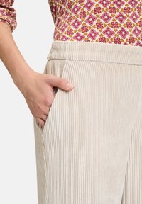 Beige ribbade kanva pantsit sivutaskujen ja joustovyön kanssa, joissa on pehmeä rakenne ja suora lahje.