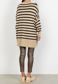 Beige en zwart gestreepte oversized trui met verlaagde schouders, geribde boorden en zijsplitten, gecombineerd met strakke bruine faux leren broeken en chunky beige schoenen.
