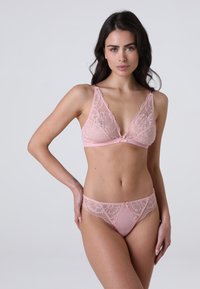 Reggiseno in pizzo e mutandine coordinate in un delicato rosa. Il reggiseno presenta dettagli in pizzo floreale e una profonda scollatura a V; le mutandine hanno accenti in pizzo.