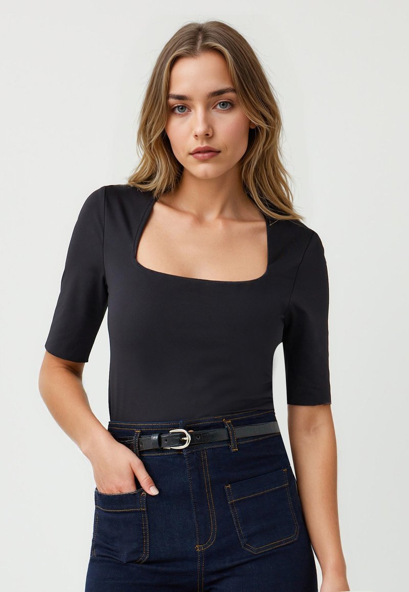 Zwarte body met vierkante halslijn en korte mouwen, gladde textuur, gecombineerd met donkere spijkerbroek met een riem. Geaccentueerd met zichtbare stiksels.