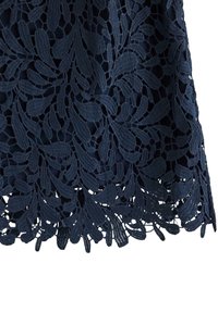 Marineblå blonderstof med et indviklet bladmønster og en bølget kant. Teksturen er detaljeret og lagdelt med en blød finish.