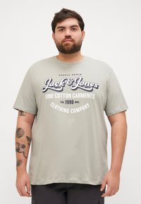 Hele rohelise puuvillase lühikeste varrukatega t-särk, millel on suur must-valge graafiline tekst: "Jack & Jones" ja "Clothing Company."