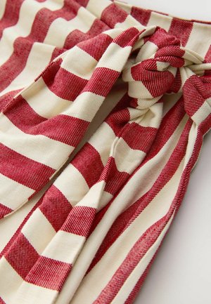 Rot- und cremefarben gestreifter Stoff mit einem geknoteten Design, einer weichen, strukturierten Oberfläche und abwechselnd breiten und schmalen Streifen.