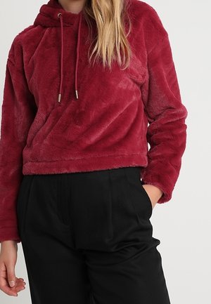 Bordeauxrode pluche hoodie met trekkoord, cropped lengte en lange mouwen; gecombineerd met zwarte taps toelopende broek. Zachte textuur en casual ontwerp.