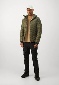 Olivo zelena napihnjena jakna s horizontalnimi šivi, oprijete črne hlače, bež srajca in siva kapa. Ima sprednjo zadrgo in žepke z zadrgo.