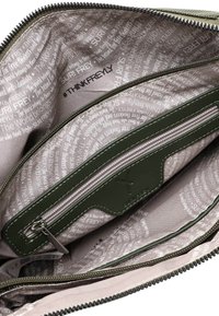 Zielony woreczek na zamek błyskawiczny z wieloma przegródkami; wnętrze wyściełane jest jasną tkaniną z wzorami tekstowymi, jedna kieszeń posiada zamek i akcent z logo.