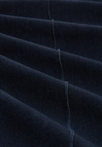 Mørkeblåt stof med en glat tekstur, der har parallelle folder og kontrasterende stikninger langs kanterne.