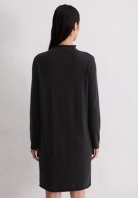 Schwarzes, langärmliges Strickkleid mit geradem Schnitt, hohem Ausschnitt und glatter Textur, das bis zur Mitte des Oberschenkels reicht und ein einfaches, minimalistisches Design zeigt.