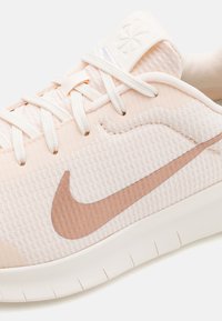 Light peach sneaker with textured fabric upper, featuring a rubber sole, white laces, and a subtle brown Nike swoosh design.