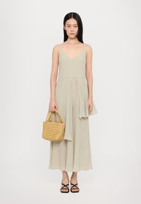 Light green pleated dress with a V-neckline and asymmetric hem. Styled with a woven tan handbag and black strappy sandals.