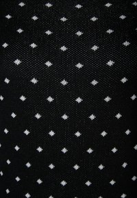 Zwarte gebreide stof met een herhalend patroon van kleine witte diamantvormen, met een textuur en regelmatige ruimte.