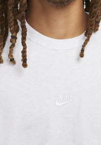 Ljusgrå bomulls t-shirt med broderad vit Nike-logotyp på bröstet. Rund hals, korta ärmar, avslappnad design.