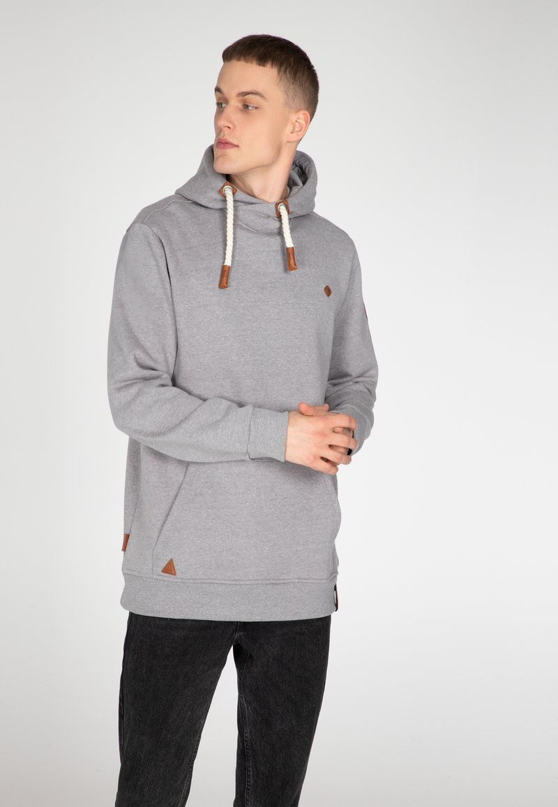 Grijze katoenen hoodie met een trekkoord, leren accenten en driehoekige patches. Heeft lange mouwen en een relaxte pasvorm, gecombineerd met zwarte jeans.