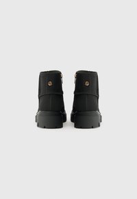 Botas pretas de cano curto feitas de tecido, com um topo acolchoado, detalhes em metal dourado e uma sola de borracha grossa com um padrão de rasto.