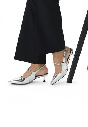 Zilveren gepatineerde leren slingback hakken met een spitse neus en smalle kittenhak, voorzien van een verstelbare riem en een gladde textuur.