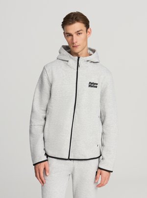 Felpa con cappuccio grigio chiaro con zip nera e dettagli neri, dotata di cappuccio e logo con testo sul petto. Tessuto morbido e strutturato con una vestibilità comoda.