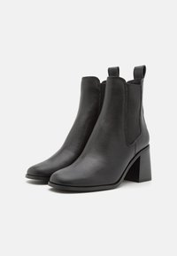 Botines de cuero negro con puntera afinada, tacón sólido, paneles laterales elásticos y detalles cosidos a lo largo de las costuras.