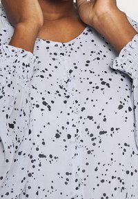 Hellgraues Button-Up-Oberteil mit schwarzen Spritzmustern, semi-transparentem Stoff, gerafften Ärmeln und rundem Halsausschnitt.