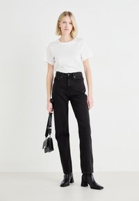 Jean noirs taille haute avec une coupe droite, associés à un t-shirt blanc à manches courtes et à des bottines à talons noires.