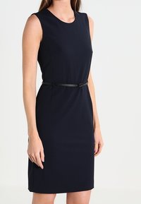 Mörkblå ärmlös klänning med en figurnära design, med rund halsringning och ett tunt svart bälte i midjan. Slät tyg, knälång.