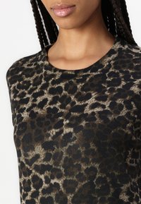 Kortermet topp med rund hals i et mykt stoff som har et brun- og svart leopardmønster. Glatt tekstur med en tettsittende silhuett.