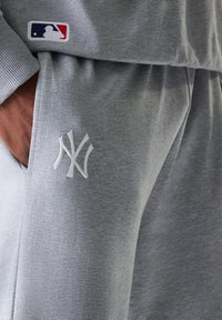 Sivé tepláky s hladkou textúrou, so štýlovým vyšitým logom "NY" v bielej farbe a nášivkou loga MLB na páse.