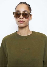 Sudadera verde con mangas raglán y un pequeño logotipo de "Marc O'Polo DENIM". Gafas de sol en forma de ojo de gato con un patrón de carey y blanco.