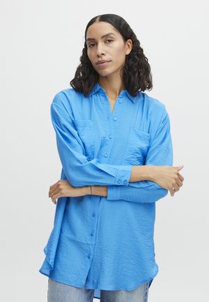 Klassisches blaues Button-Down-Hemd mit strukturiertem Finish, ausgestattet mit einem Kragen, zwei Fronttaschen und langen Ärmeln, ergänzt durch einen abgerundeten Saum.