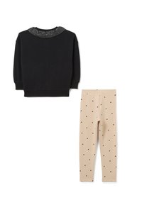 Zwarte sweatshirt met een fonkelende, met studs versierde kraag, gecombineerd met beige leggings met kleine zwarte stippen.