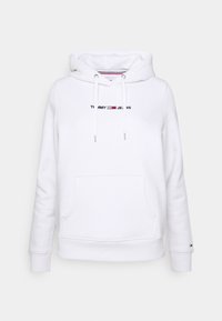 Valkoinen huppari etutaskulla, jossa on mustalla brodeerattu "TOMMY JEANS". Narut metallisin päihin ja ribbireunat.