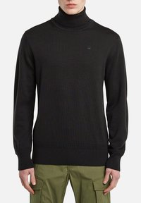 Schwarzer Rollkragenpullover aus geripptem Stoff mit eng anliegenden Ärmeln und feiner Struktur. Verfügt über ein kleines Markenlogo auf der Brust.