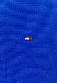 Tessuto blu con una trama liscia, caratterizzato da un piccolo logo ricamato con strisce orizzontali rosse, bianche e blu navy.