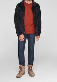 Granatowa kurtka sztruksowa na czerwonym swetrze o fakturze, w połączeniu z ciemnymi dżinsami i beżowymi botkami na sznurowadła z czerwonymi sznurówkami.