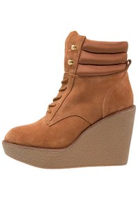 Beżowe zamszowe botki na klinie z wyściełanym kołnierzem, sznurowane od przodu, z złotymi oczkami i teksturowaną platformą.