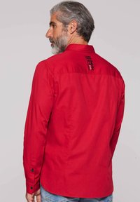 Rotes Langarmhemd mit Button-Down-Kragen, verstellbaren Manschetten und einem grafischen Druck auf dem oberen Rücken. Glattes Baumwollmaterial.